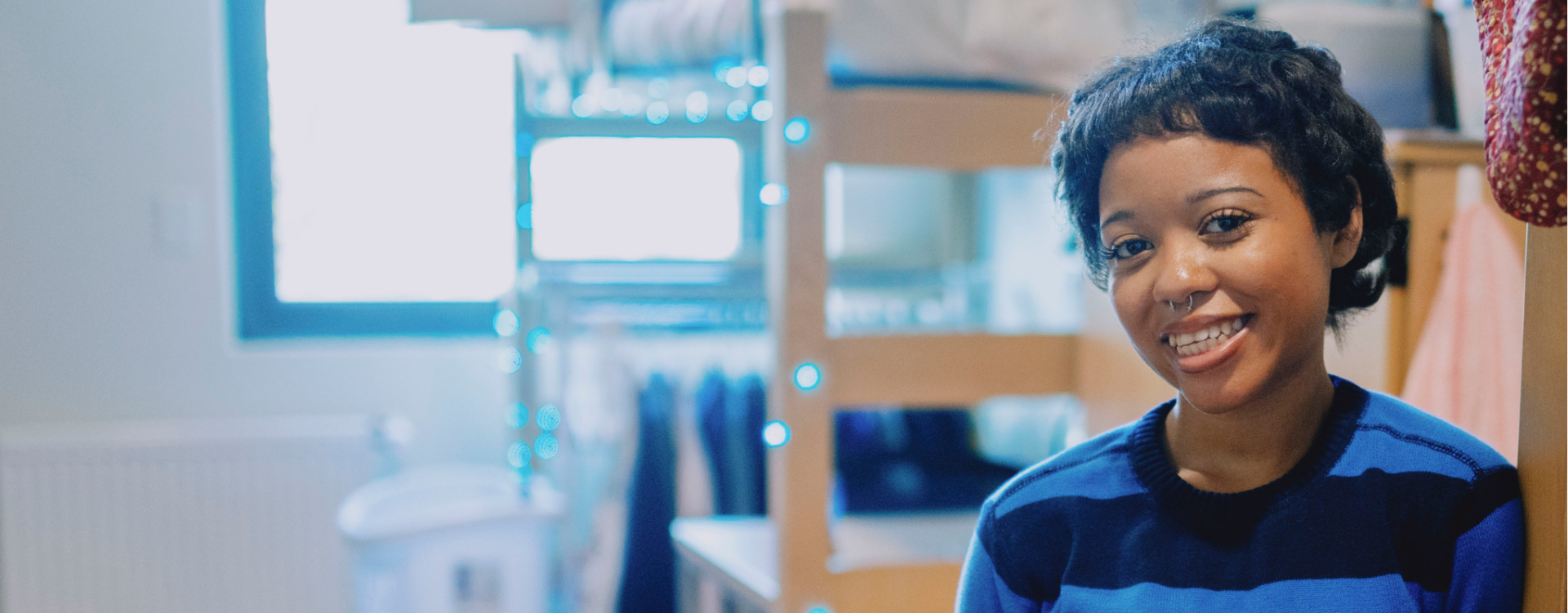Student smiling in dorm room with bed in the background