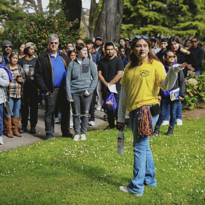 Student tour guide in speaking to group tour on green campus lawn