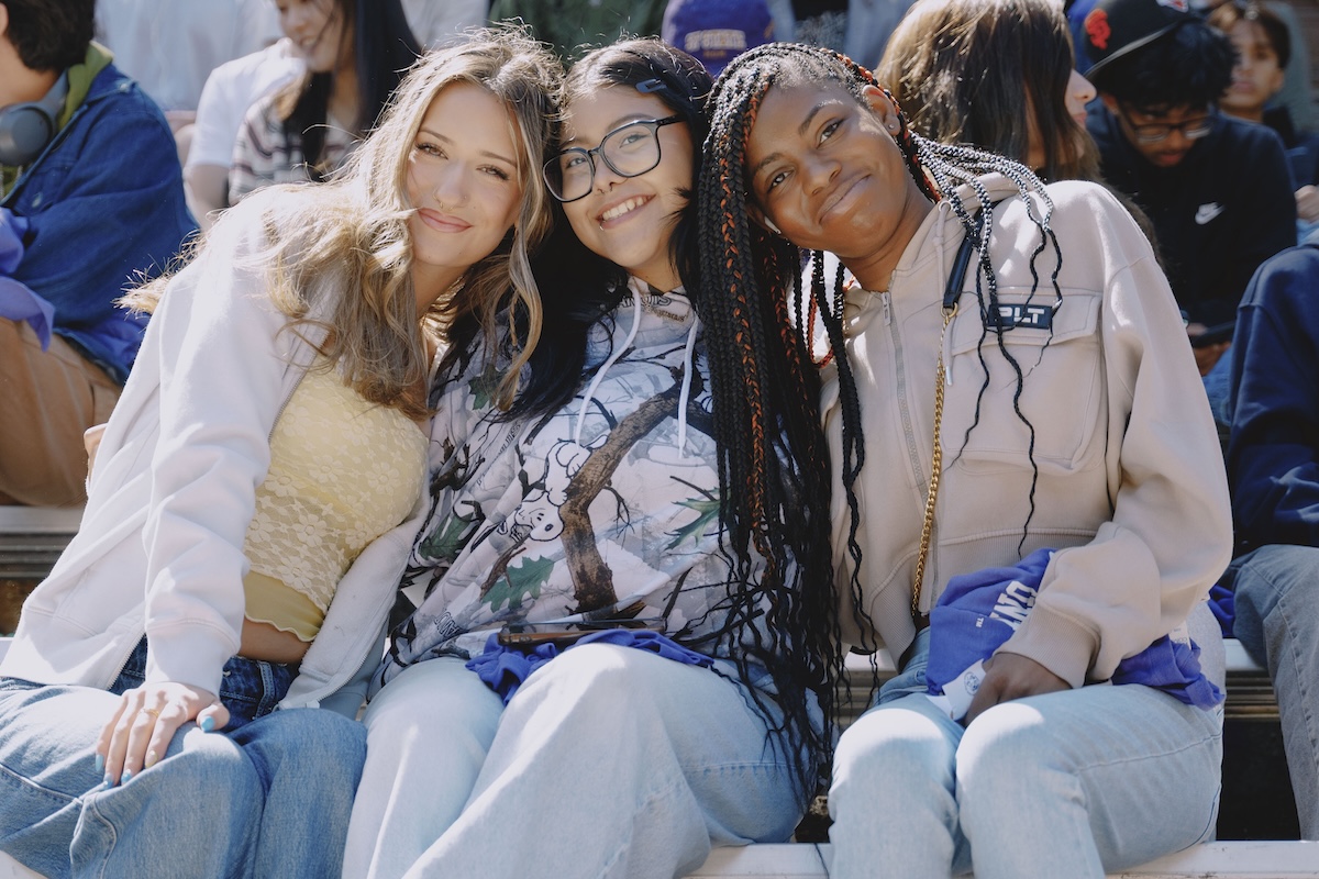 Three female students sitting in bleachers on a sunny day